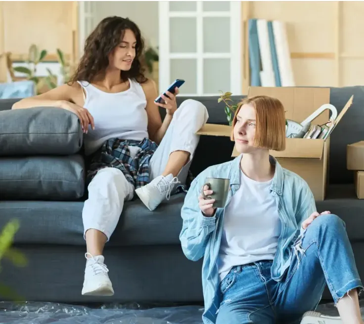 Due ragazze sedute in salotto, una guarda il telefono