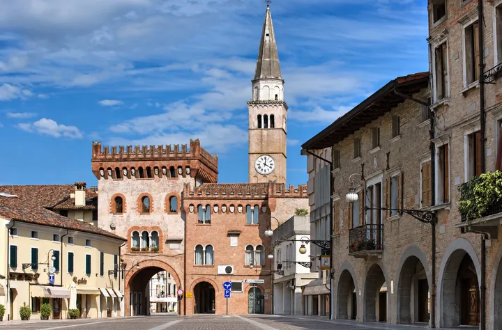Una coppia sorridente in piazza del Popolo a San Vito al Tagliamento, con la Torre Raimonda e il campanile
